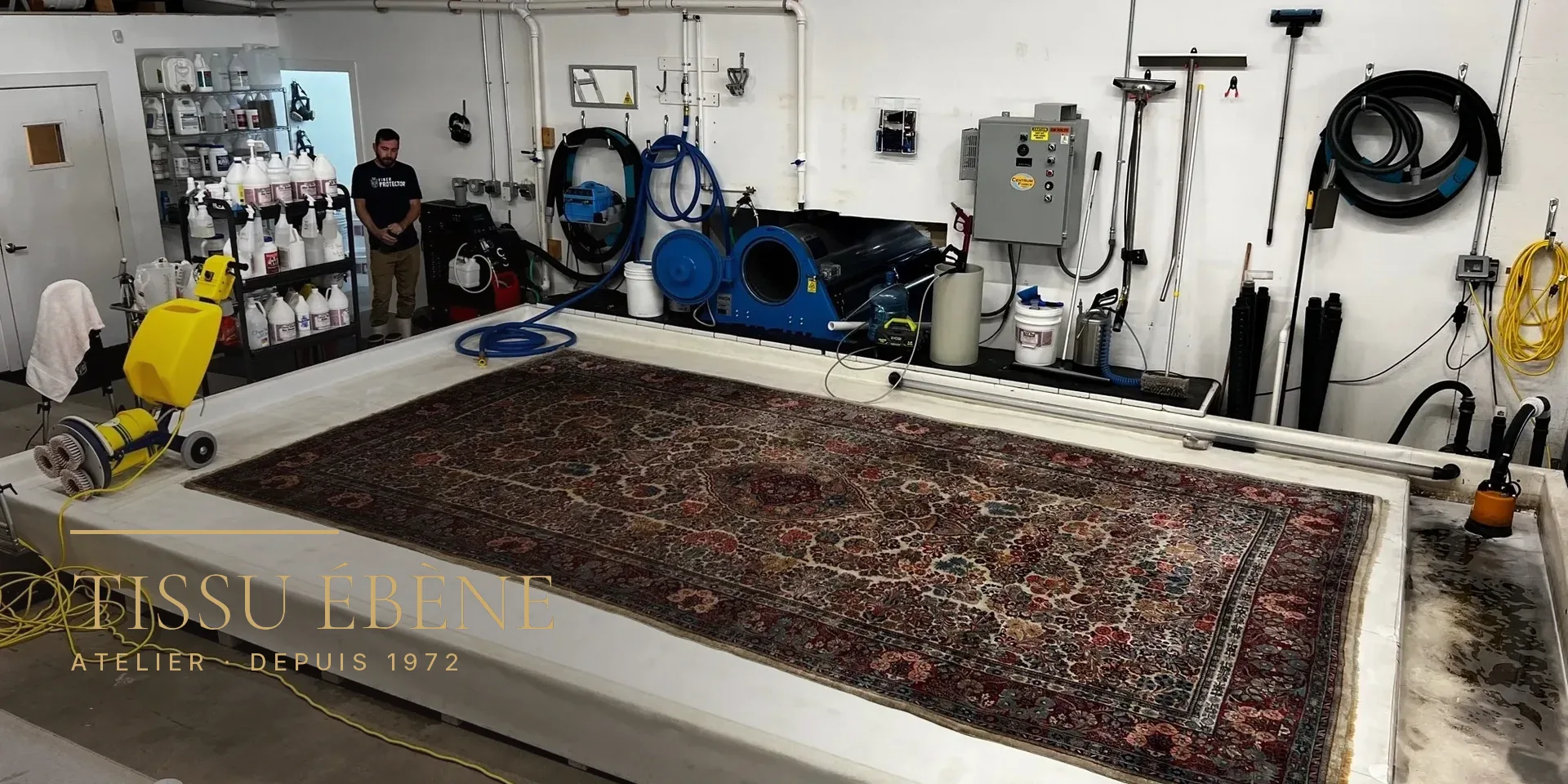 Grand tapis d&rsquo;Orient à médaillon étendu sur une table de lavage dans un atelier équipé de machines