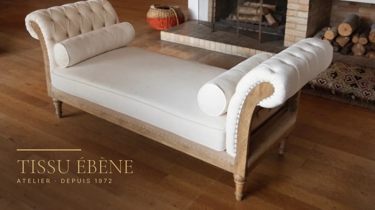 Banquette capitonnée en tissu ivoire avec deux traversins, piètement en bois clair, devant une cheminée