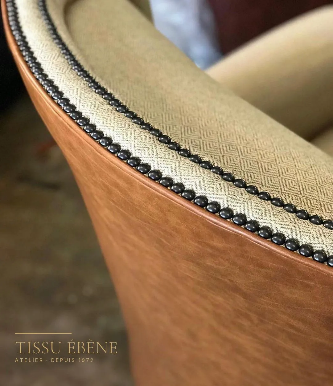Détail d’un dossier de fauteuil cuir fauve et tissu beige à losanges, souligné de clous noirs