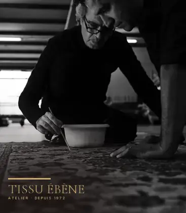 Artisan posant une teinte au pinceau sur un tapis, à l’atelier