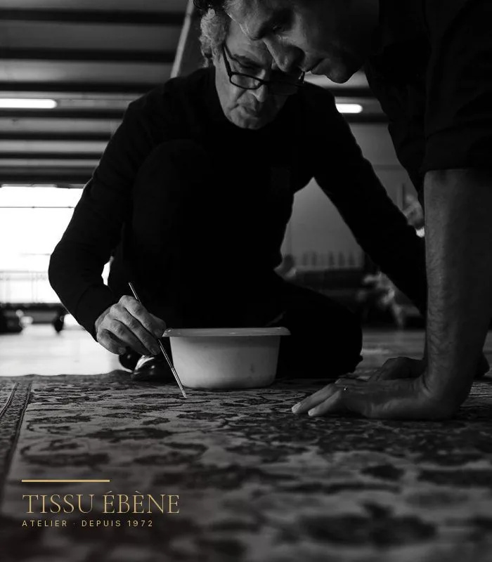 Artisans agenouillés sur un tapis persan pour raviver une couleur au pinceau