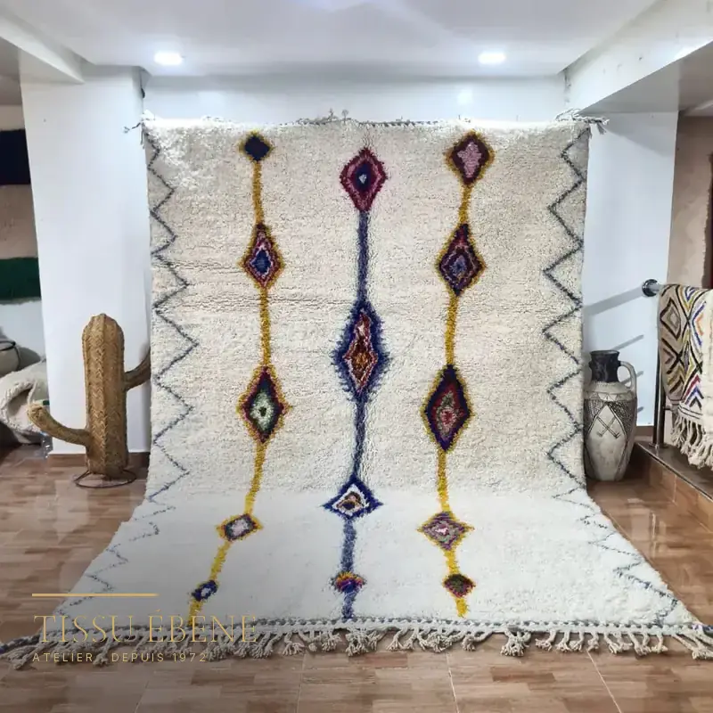 Tapis berbère blanc à losanges colorés et zigzags, suspendu dans une boutique au sol carrelé