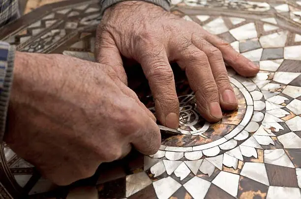Artisan recollant les tesselles de nacre d'un plateau marqueté