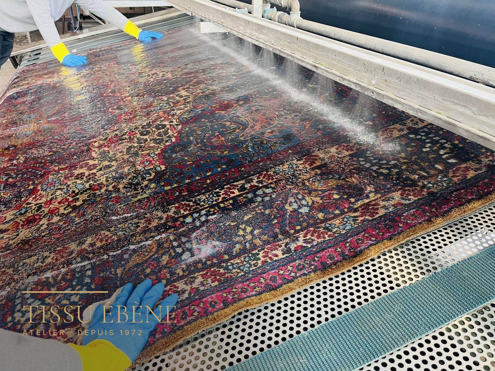 Tapis persan rincé à l’eau claire, à plat, sur la table de lavage de l’atelier
